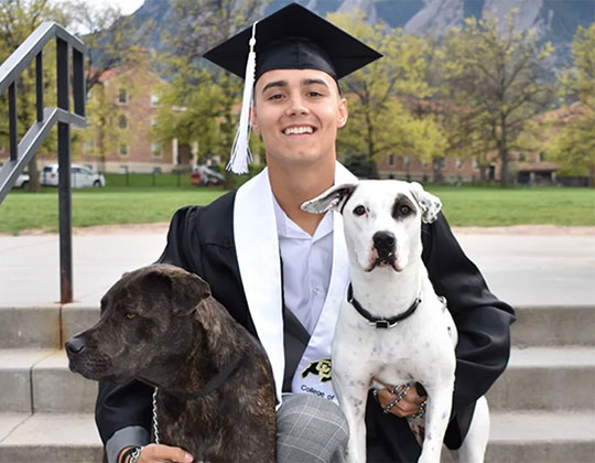 Alex McCarl - Co Owner and General Manager of The Pet Spot in Boulder Colorado wearing a graduation cap and holding two dogs